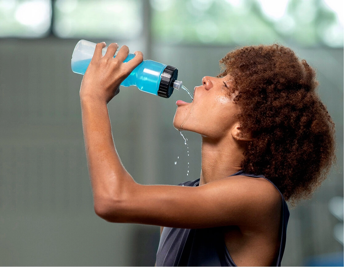 A young man squirting Sqwincher into his mouth during a break in a workout